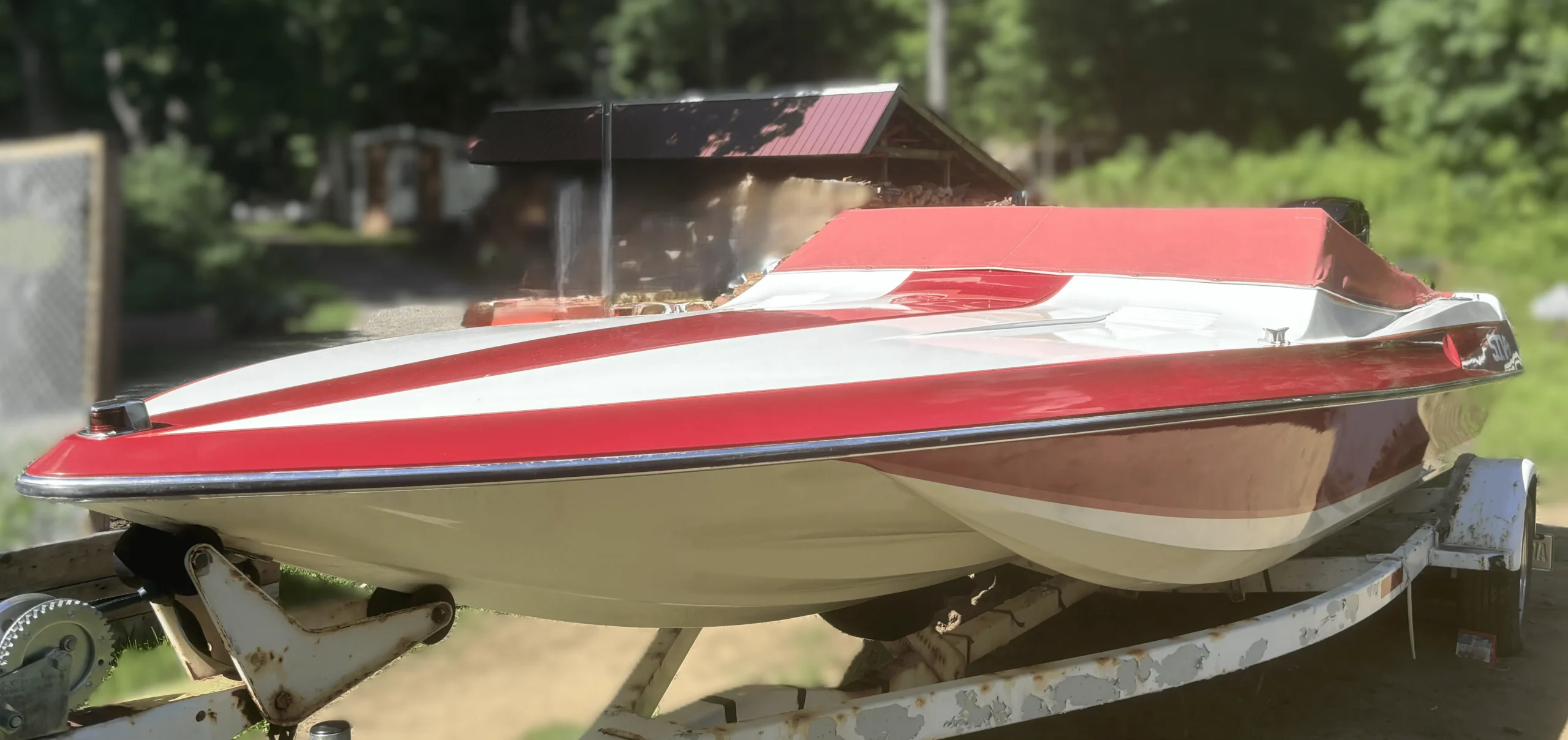 Shiny red and white STV boat with a dull red cover on a rusty trailer, showcasing its polished hull after True North Detailing Muskoka service.